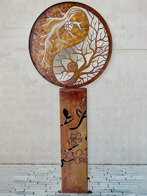 A large, intricate yin yang forest metal sculpture stands prominently, showcasing its artistic design